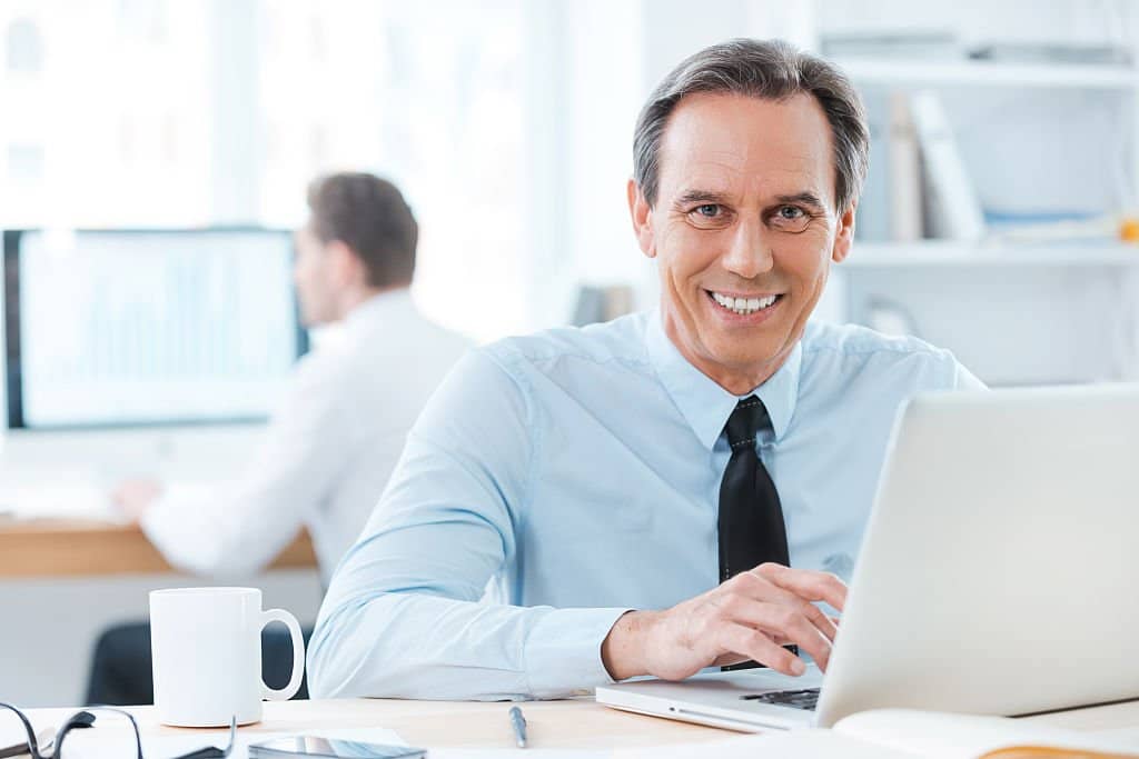 Smiling businessman working on a laptop in a bright office.