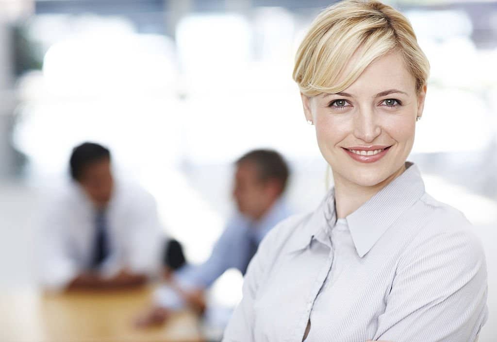 Confident businesswoman smiling with colleagues in the background.