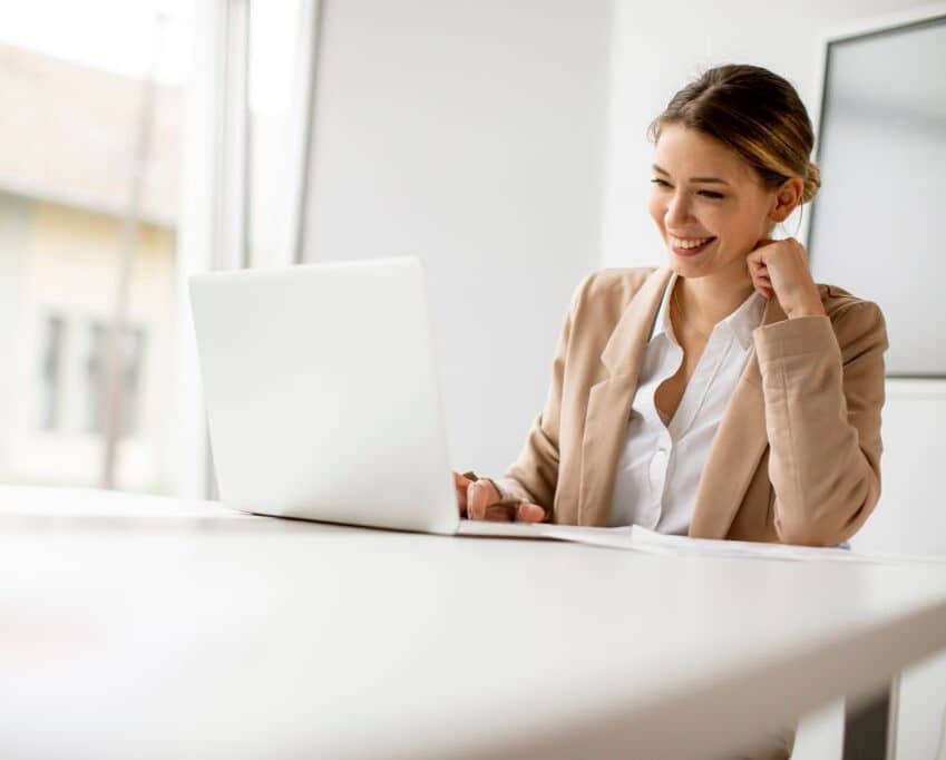 Smiling businesswoman working on a laptop in a bright office.